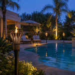 Gothic-style tiki torches glowing around a backyard pool at dusk